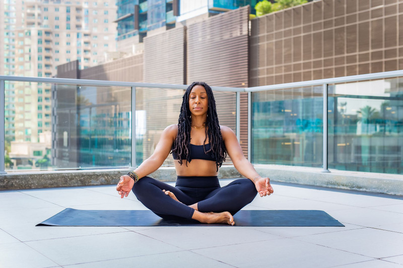 A woman meditating on a yoga mat on a city balcony.
