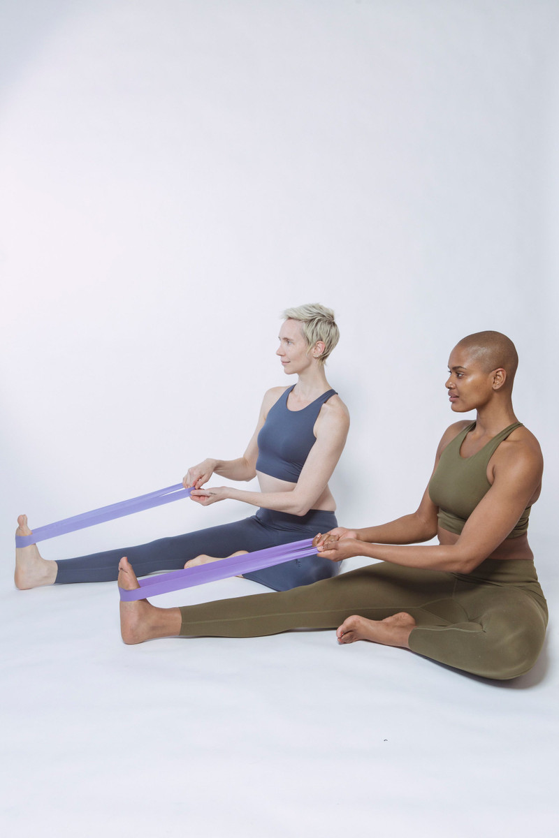 Two women stretching with fabric bands on the floor.