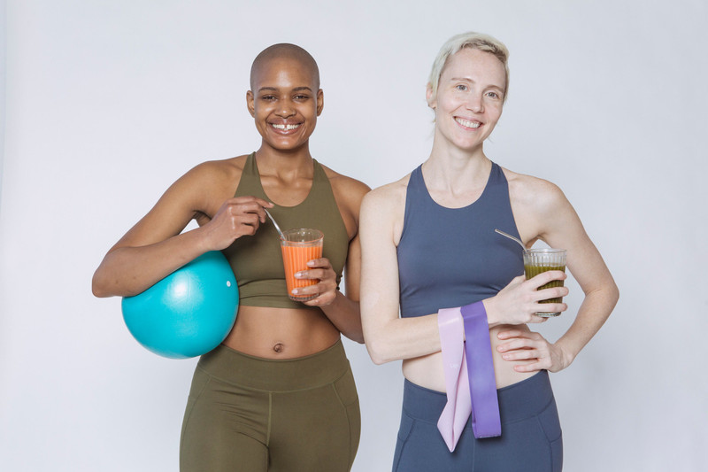 Two women in matching activewear with a gym ball and smoothies.